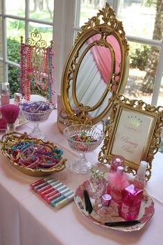 a table topped with lots of pink and gold items next to a mirror on top of a white table cloth