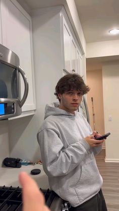 a young man standing in a kitchen holding a cell phone and pointing at the camera