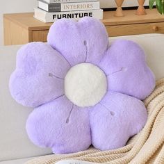 a purple flower pillow sitting on top of a white couch next to a stack of books