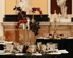 a table set up with wine glasses, candles and flower centerpieces in front of a fireplace