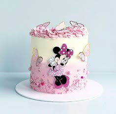 there is a pink and white cake with minnie mouse decorations on the top, along with butterflies