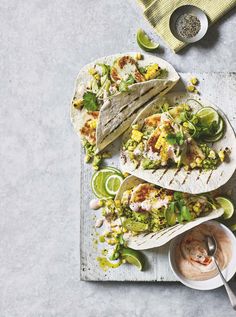 three tacos with guacamole, corn and salsa on a wooden board