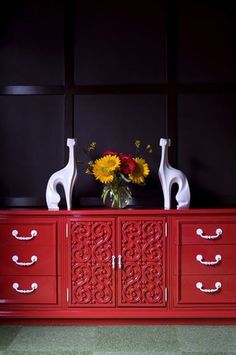 a red dresser with two vases and flowers on top