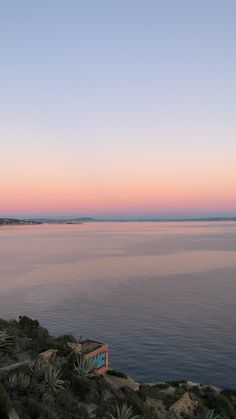 a body of water sitting next to a lush green hillside under a blue sky at sunset