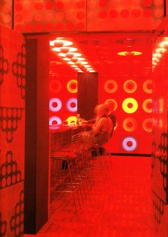 a woman sitting at a bar in a red room with circles painted on the walls