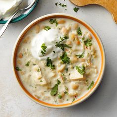 a bowl of soup with sour cream and parsley on the side next to a spoon