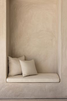 a white couch with two pillows on it in a room that is made out of concrete