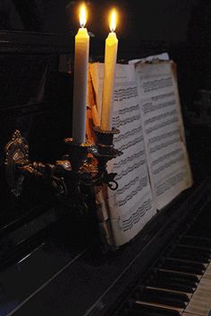 two lit candles are sitting on top of an open book next to a piano keyboard