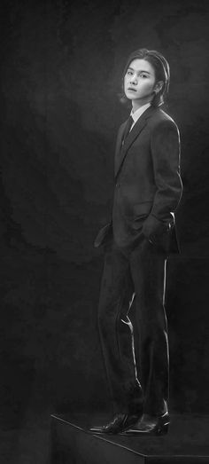 a black and white photo of a young man in a suit standing on a pedestal