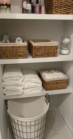 an organized bathroom closet with baskets and towels