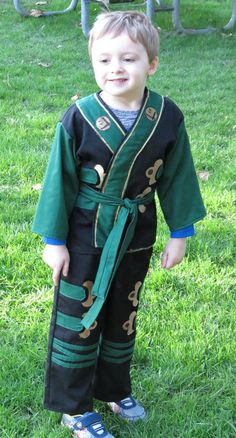 a young boy wearing a green and black robe standing in the grass with his shoes on