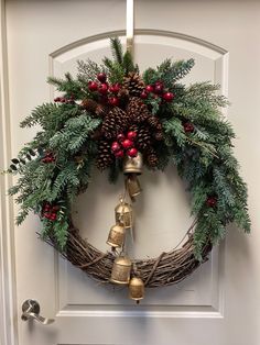 a christmas wreath hanging on the front door with bells and evergreen leaves, red berries and pine cones