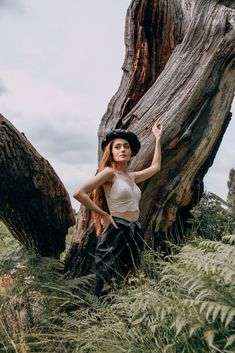 a woman with long red hair standing in front of a tree wearing a cowboy hat