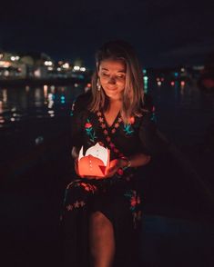 a woman holding an origami box in her hands at night by the water