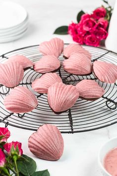 some pink cookies are on a cooling rack with flowers next to it and two white plates