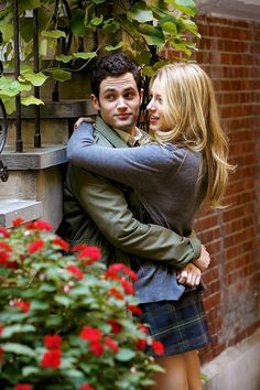 a young man and woman embracing each other in front of a flower pot with red flowers