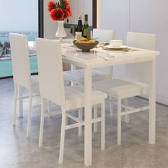 a white table with four chairs and a bowl of fruit on it in front of a large window