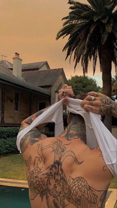 a man with tattoos on his back is holding up a white shirt over his head