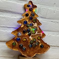 a christmas tree made out of glass beads on top of a wooden stand against a white brick wall