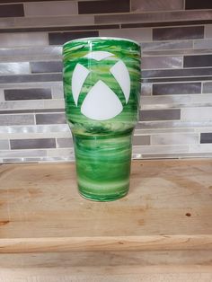 a green and white cup sitting on top of a wooden table next to a tile wall