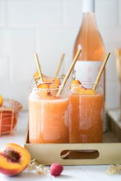 two glasses filled with orange juice on top of a table next to some peaches