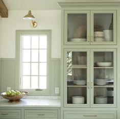 a kitchen with green cupboards and white counter tops in front of a bowl of fruit