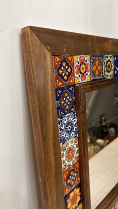 a mirror that is on the wall near a wooden frame with an artistic design painted on it