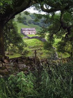 an old stone house in the middle of a green field with trees and grass around it