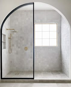 an arched glass shower door in a white tiled bathroom with tile flooring and walls