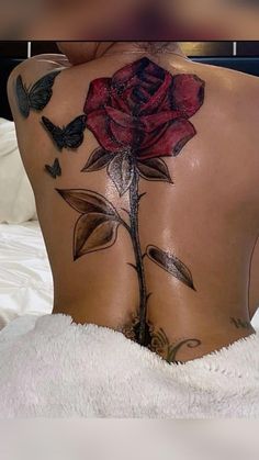 the back of a woman's body with tattoos on it and a rose tattoo