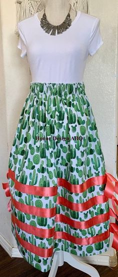 Traditional ribbon skirt in bright green cactus print with coral hanging ribbon.  Finished with elevated details such as coral pink satin ribbon, lovingly made by hand. A paper bag waist hugs the body, while also being comfortable to wear. See our sizing details below to find your perfect size.  Ready to ship! A long time symbol femininity, sisterhood and solidarity, used in ceremony and everyday, every skirt tells a story written by the woman who wears it. Perfect for every season, dressed up o Ribbon Skirts Native American Top, Time Symbol, Indigenous Artwork, Beaded Pins, 4h Projects, Paper Bag Design, Ribbon Skirt, Ribbon Skirts, Green Cactus