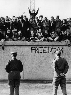 black and white photograph of people standing in front of a wall with graffiti on it