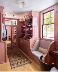 a room with pink walls and wooden flooring has a bench, chair, and closet