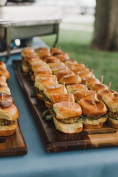 many sandwiches are on wooden trays with toothpicks in the shape of sliders