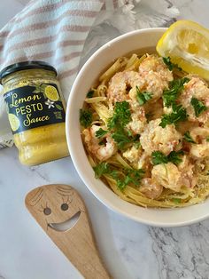 a bowl of pasta with shrimp and parsley next to a jar of lemon pesto sauce