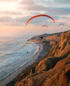 two parasailers are flying over the ocean on a cliff near the beach at sunset