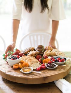 a woman standing in front of a wooden platter filled with fruit and breads