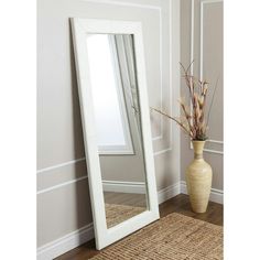 a white floor mirror sitting on top of a wooden floor next to a vase filled with flowers