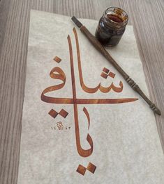 an arabic calligraphy is displayed on a piece of paper next to a paintbrush