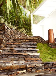 a pile of rocks sitting on top of a lush green hillside next to a building