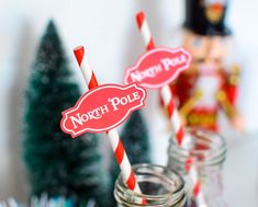 two mason jars with red and white striped paper straws in front of christmas trees