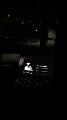 an open laptop computer sitting on top of a desk next to a window at night