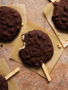 three chocolate covered cookies on top of brown paper with wooden stick sticking out of them