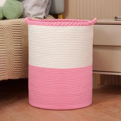 a pink and white basket sitting on top of a wooden floor next to a bed