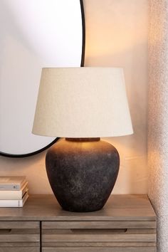 a table lamp sitting on top of a wooden dresser next to a round shaped mirror