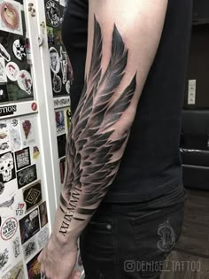 a man with a black and grey tattoo on his arm that has an angel wing