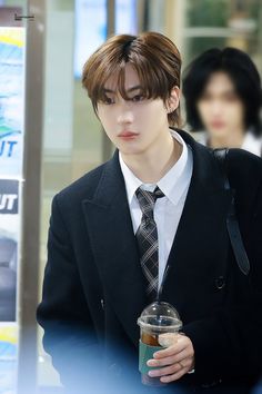 a young man wearing a suit and tie holding a coffee cup in his right hand