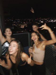 four girls are posing for the camera in front of a cityscape at night