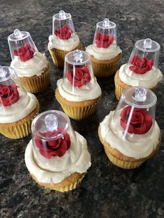 twelve cupcakes with frosting and red rose decorations on them sitting on a table