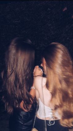 two young women are talking on their cell phones outside in the dark, one is wearing a white tank top and black leather pants